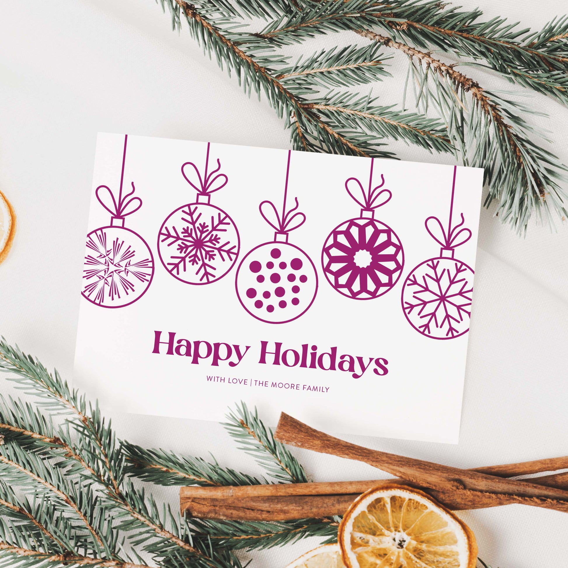 Personalized holiday card with hanging ornaments styled with greenery, cinnamon sticks, and dried oranges.
