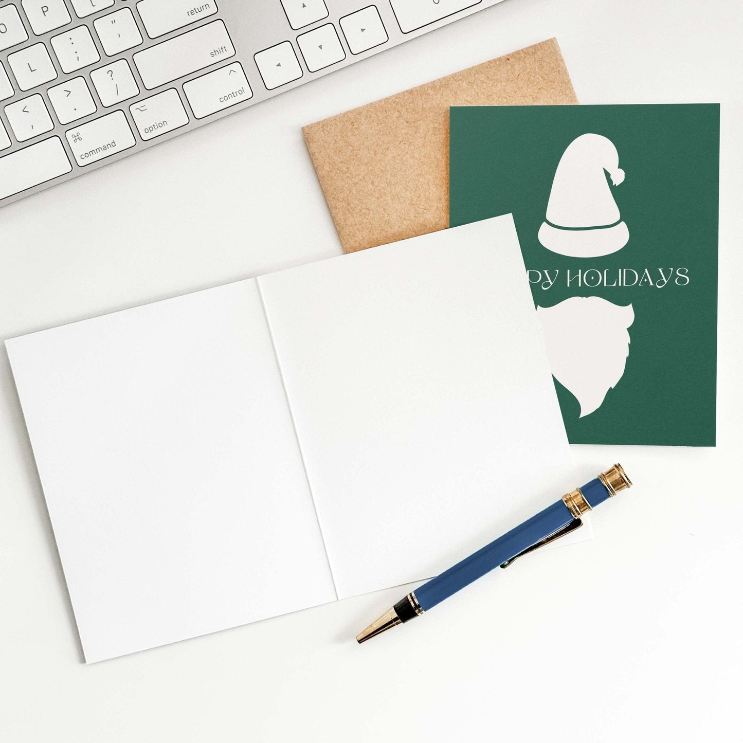 Flat lay of eco-friendly Santa holiday greeting card with blank inside, kraft envelope, and pen on desk