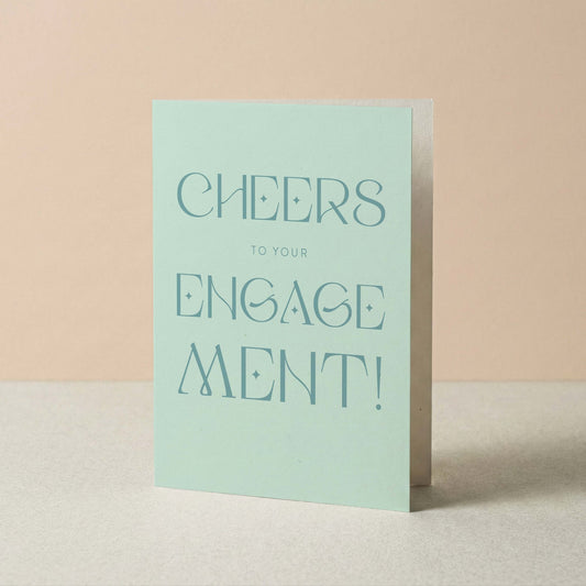 Light blue card with 'Cheers to your engagement!' text on a beige background