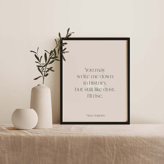 Framed artwork with a quote by Maya Angelou on a table with decorative vases and plants.