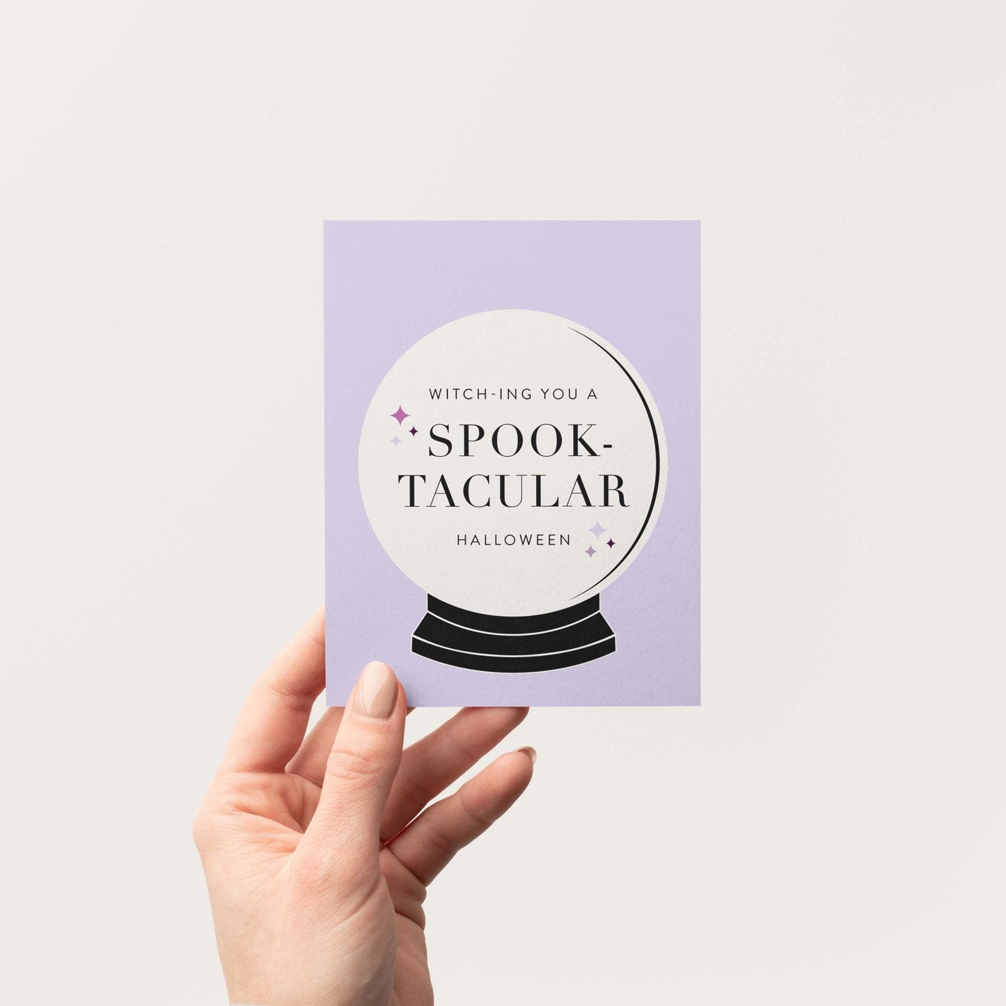 Person holding Spooktacular Halloween greeting card with crystal ball illustration and bold modern typography.