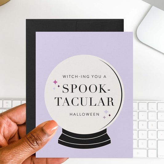 Halloween greeting card with crystal ball design styled on desk with black envelope and computer keyboard.
