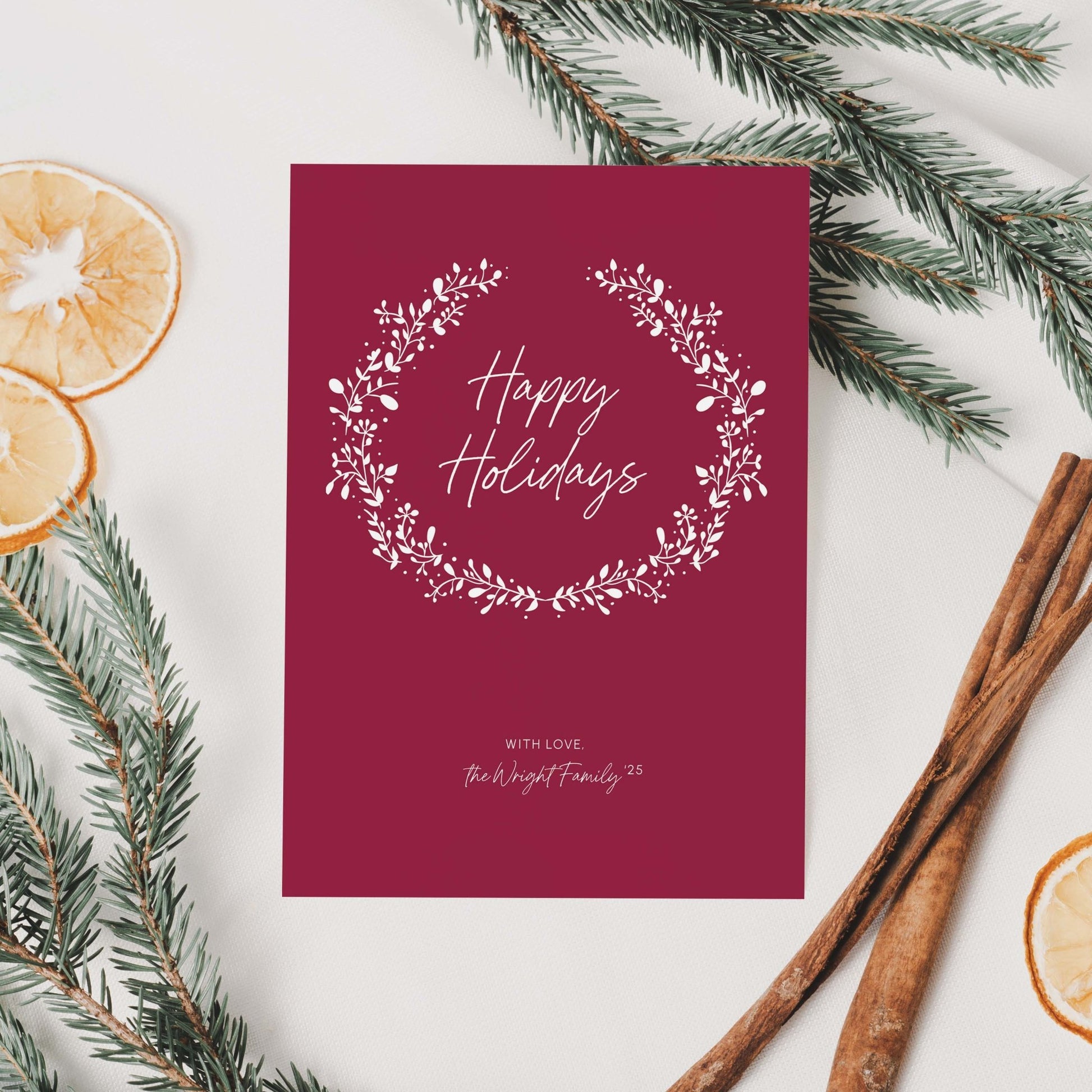 Personalized red holiday card with white wreath styled with dried oranges, pine branches, and cinnamon sticks.