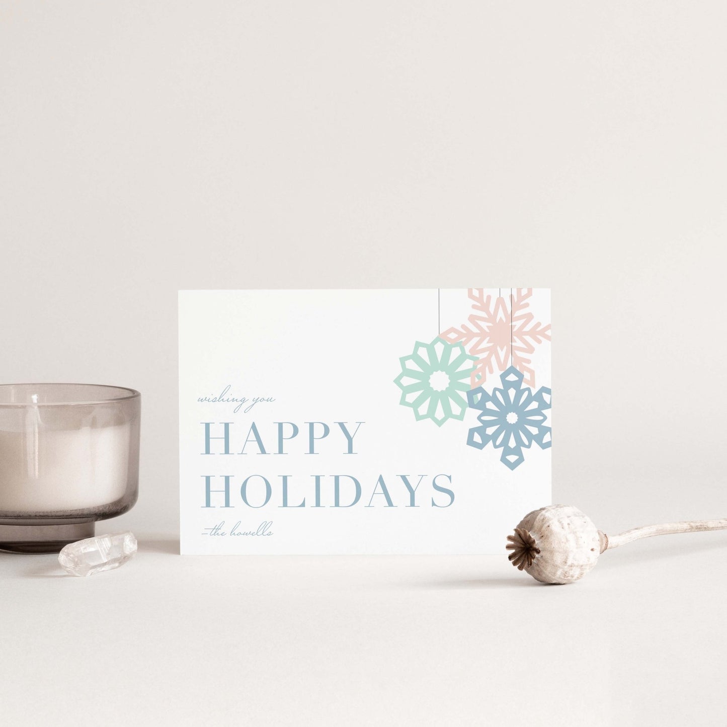 Minimal holiday card styled with a candle, gem, and dried floral on a soft neutral background.