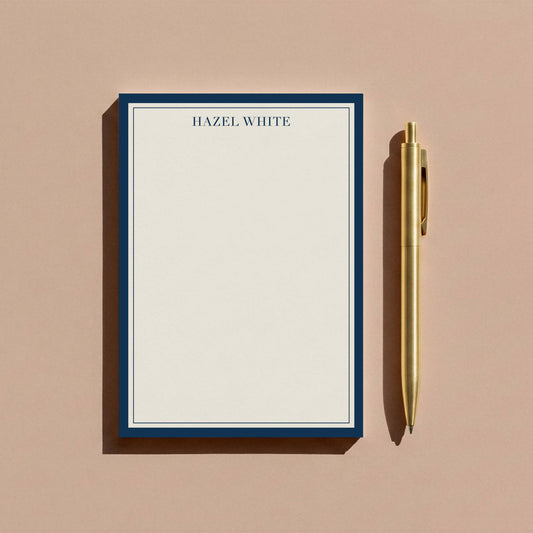 Navy skinny border notepad styled with gold pen on warm tan surface.