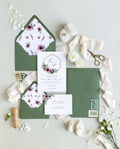 Moody Genevieve wedding invitation suite by Blú Rose, invitation and reply card with a copper geometric frame and mauve florals, styled with sage green envelopes, floral liners, ribbon, and a wax seal