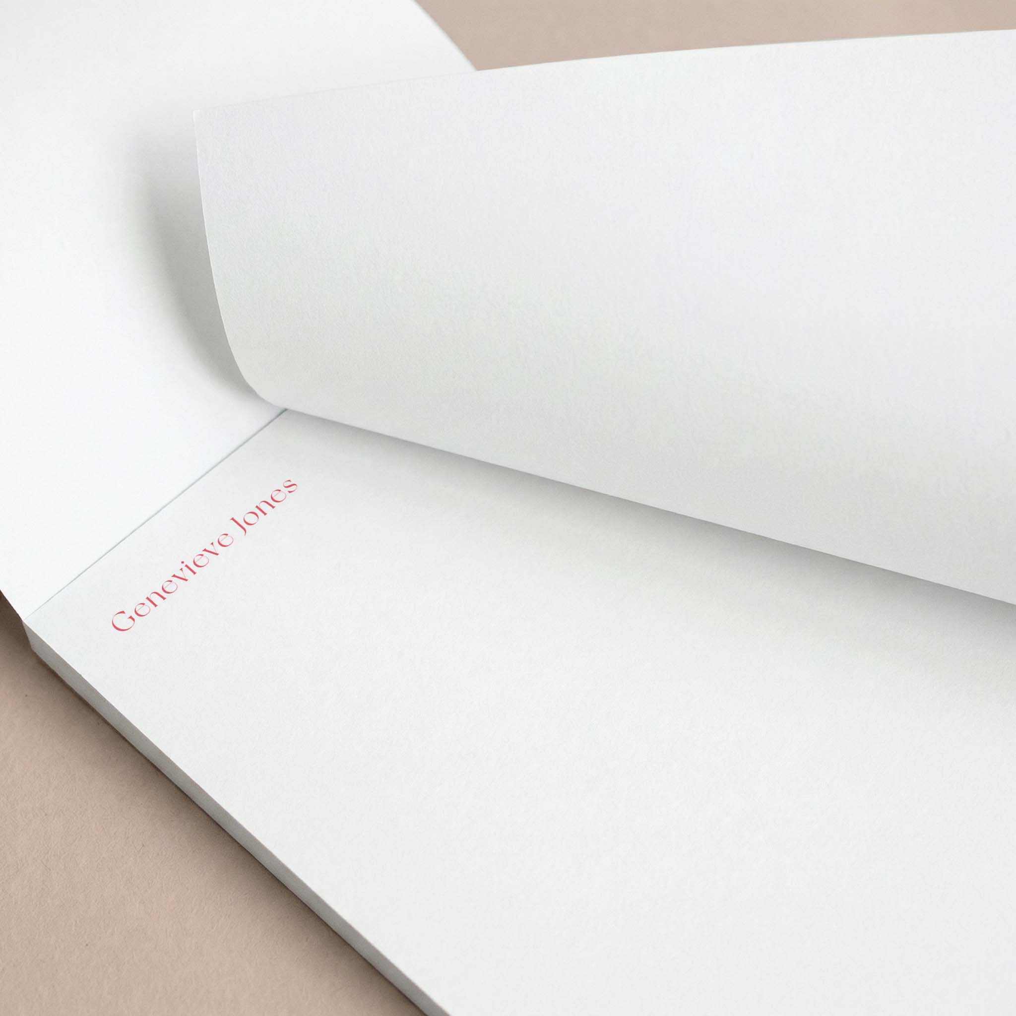 Genevieve stationery set by Blú Rose, close-up of the notepad with the top sheet lifted showing 'Genevieve Jones' in coral