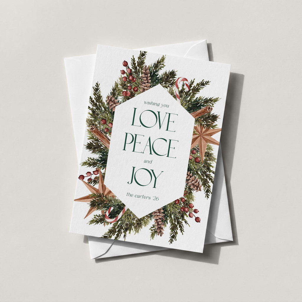 Winter Wreath holiday card with an evergreen, pinecone and berry wreath framing LOVE PEACE and JOY in green lettering
