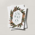 Winter Wreath holiday card with an evergreen, pinecone and berry wreath framing LOVE PEACE and JOY in green lettering