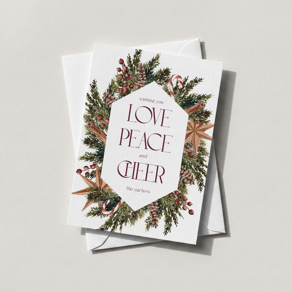 Winter Wreath holiday card with an evergreen, pinecone and berry wreath framing LOVE PEACE and CHEER in burgundy lettering