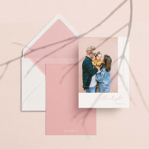All is Bright photo card with its dusty rose envelope liner styled on a blush backdrop