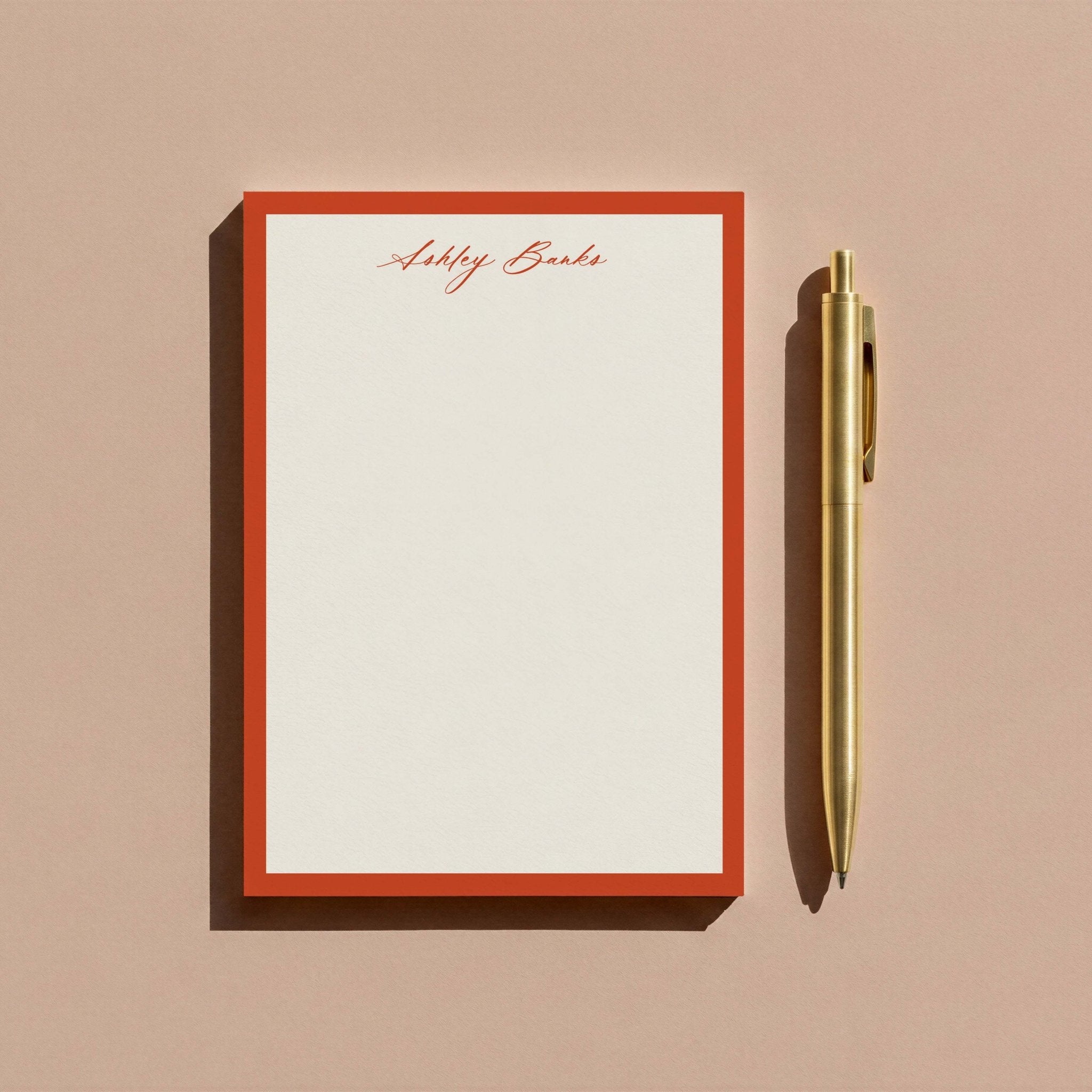 Ashley Border personalized notepad by Blú Rose, rust-bordered notepad photographed with a gold pen on a mauve background