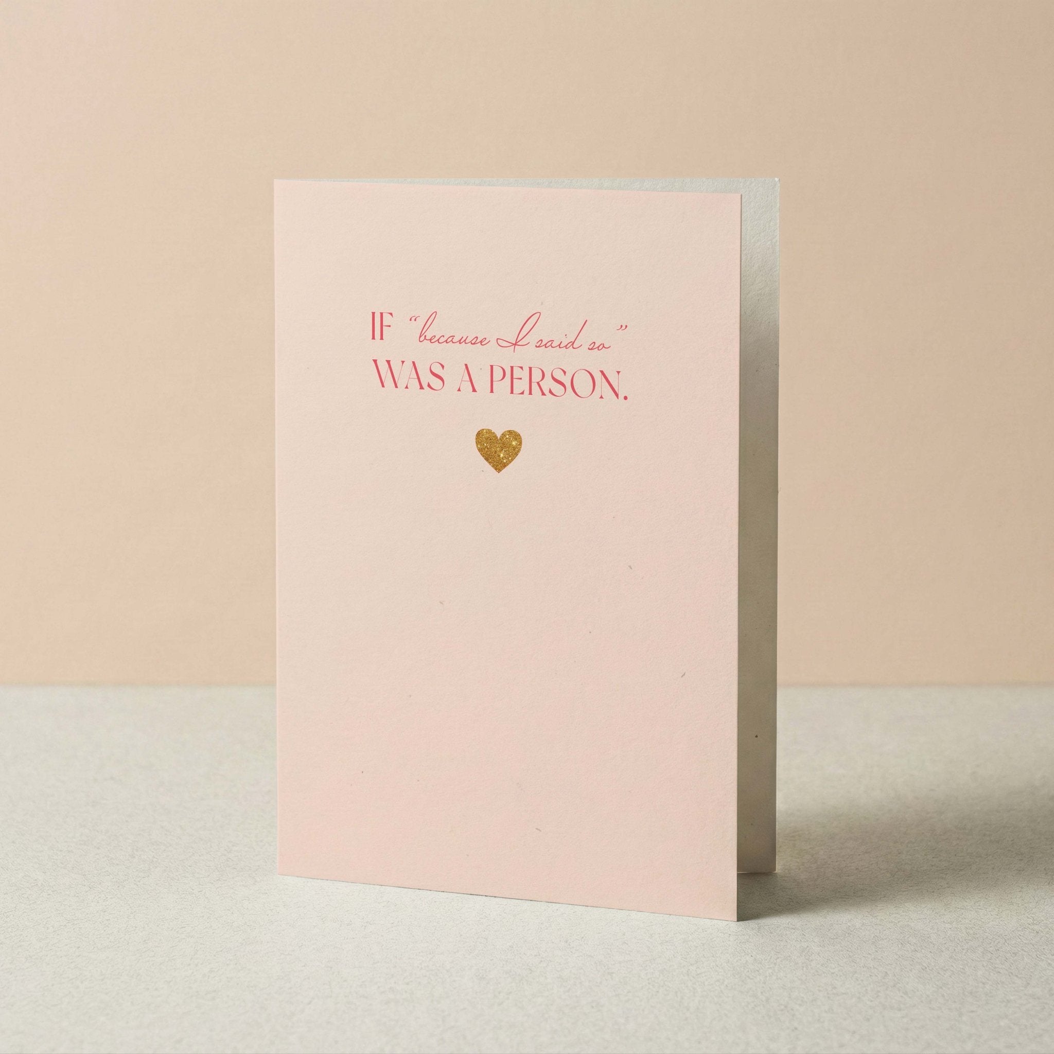 A light pink greeting card with the phrase 'IF because I said so WAS A PERSON.' in pink lettering and a small gold heart, standing upright on a light surface against a soft beige background.