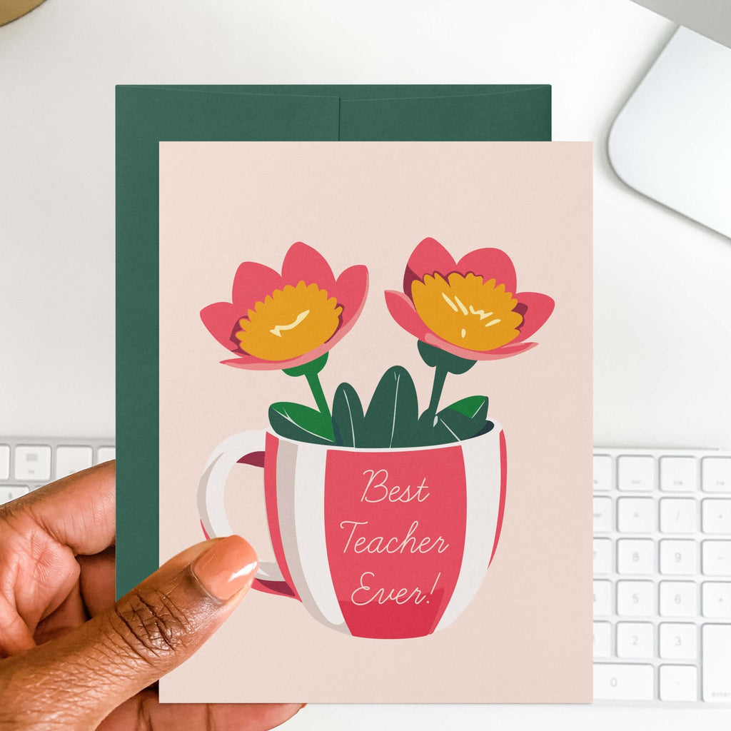 Best Teacher Ever teacher greeting card by Blú Rose held in hand over a white desk with keyboard and green envelope