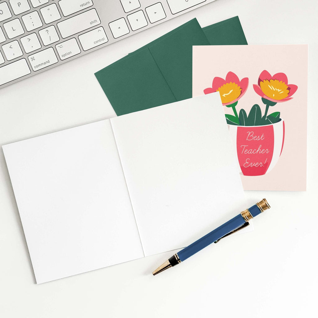 Best Teacher Ever teacher card by Blú Rose shown open with blank interior, green envelopes and pen on a white desk