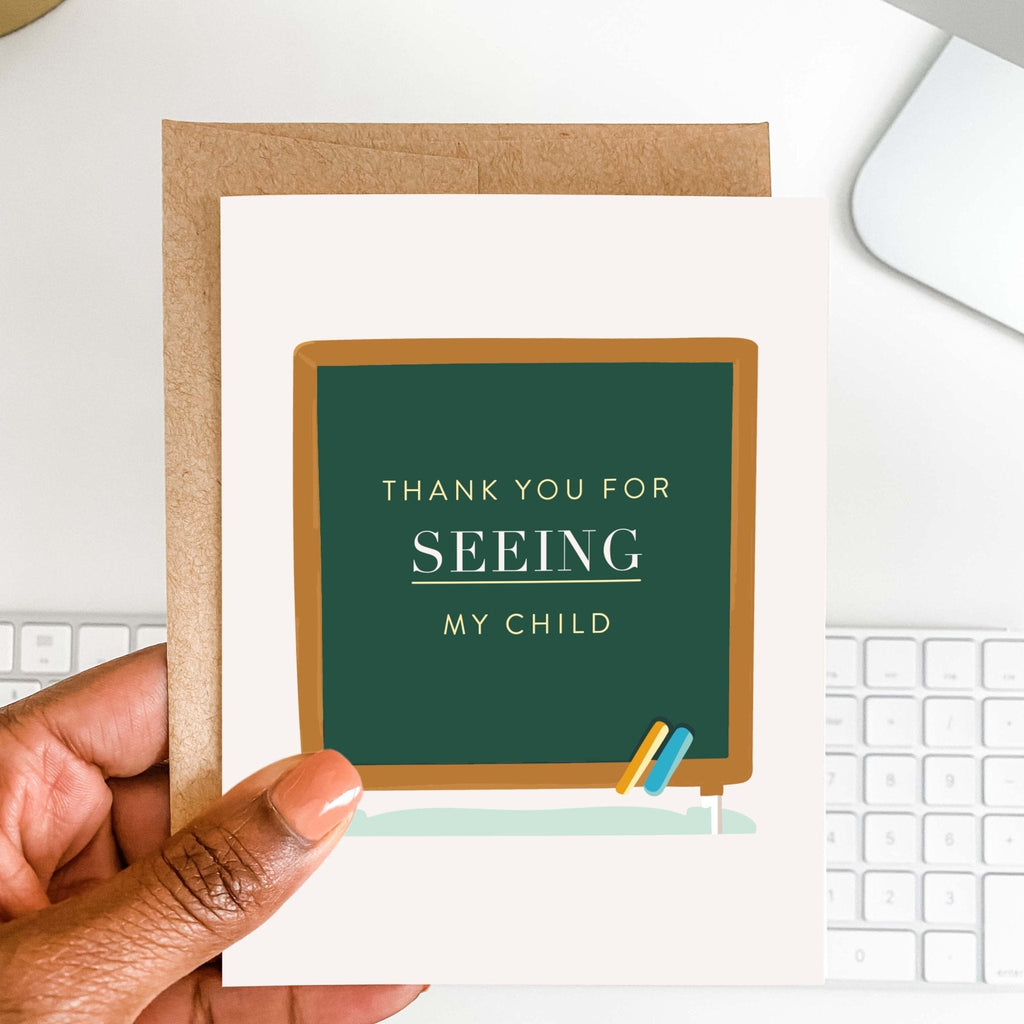 Chalkboard Tribute teacher thank you card by Blú Rose held in hand over a white desk with keyboard and kraft envelope