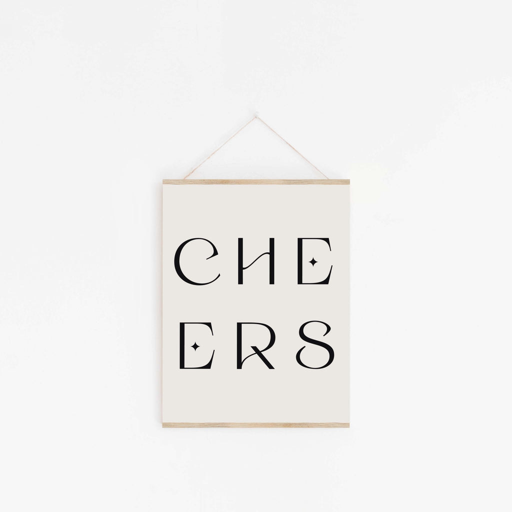Minimal “CHEERS” typography art print with black lettering hanging on a white wall with wooden poster rails.