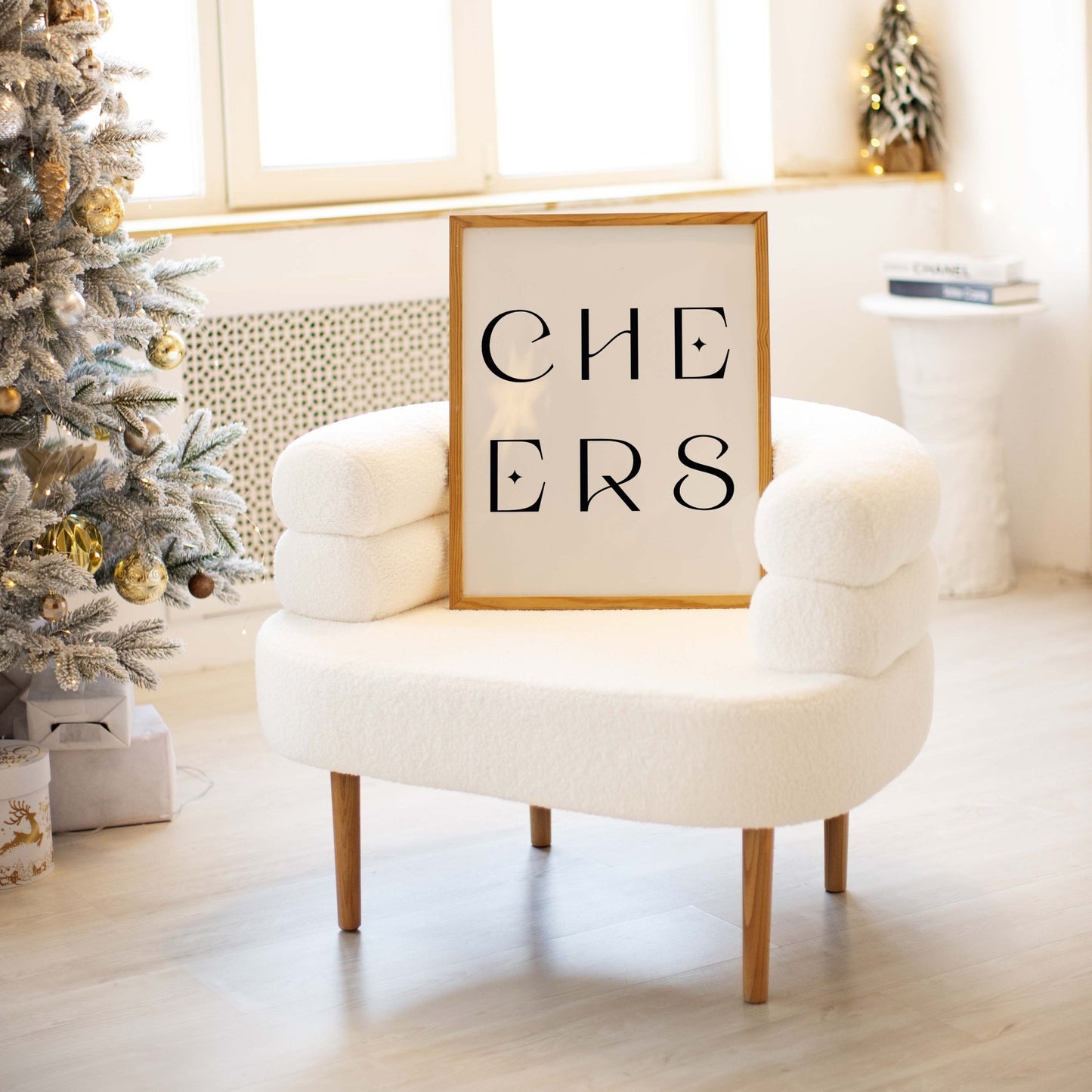 Neutral “CHEERS” art print displayed on a chair in a bright living space with holiday decor.