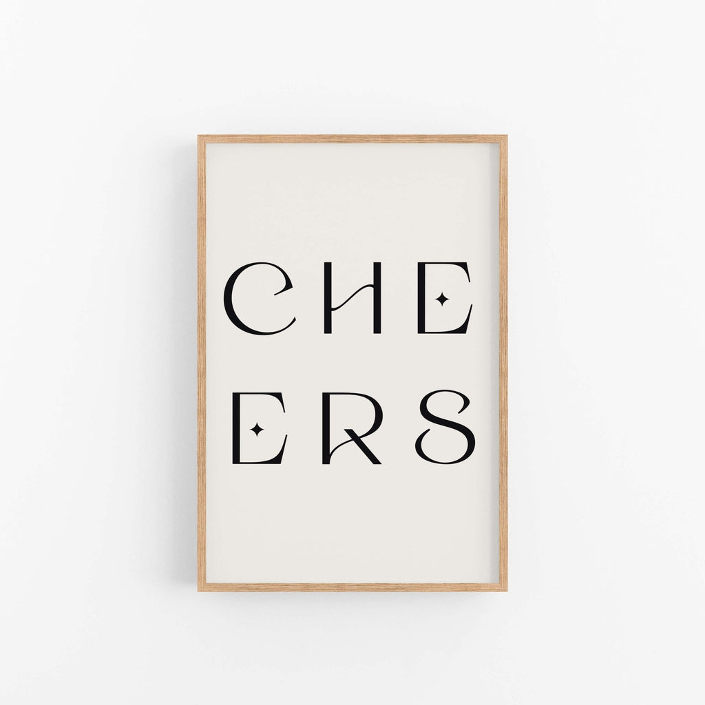 Minimal “CHEERS” typography art print with black lettering in a wood frame on white wall.