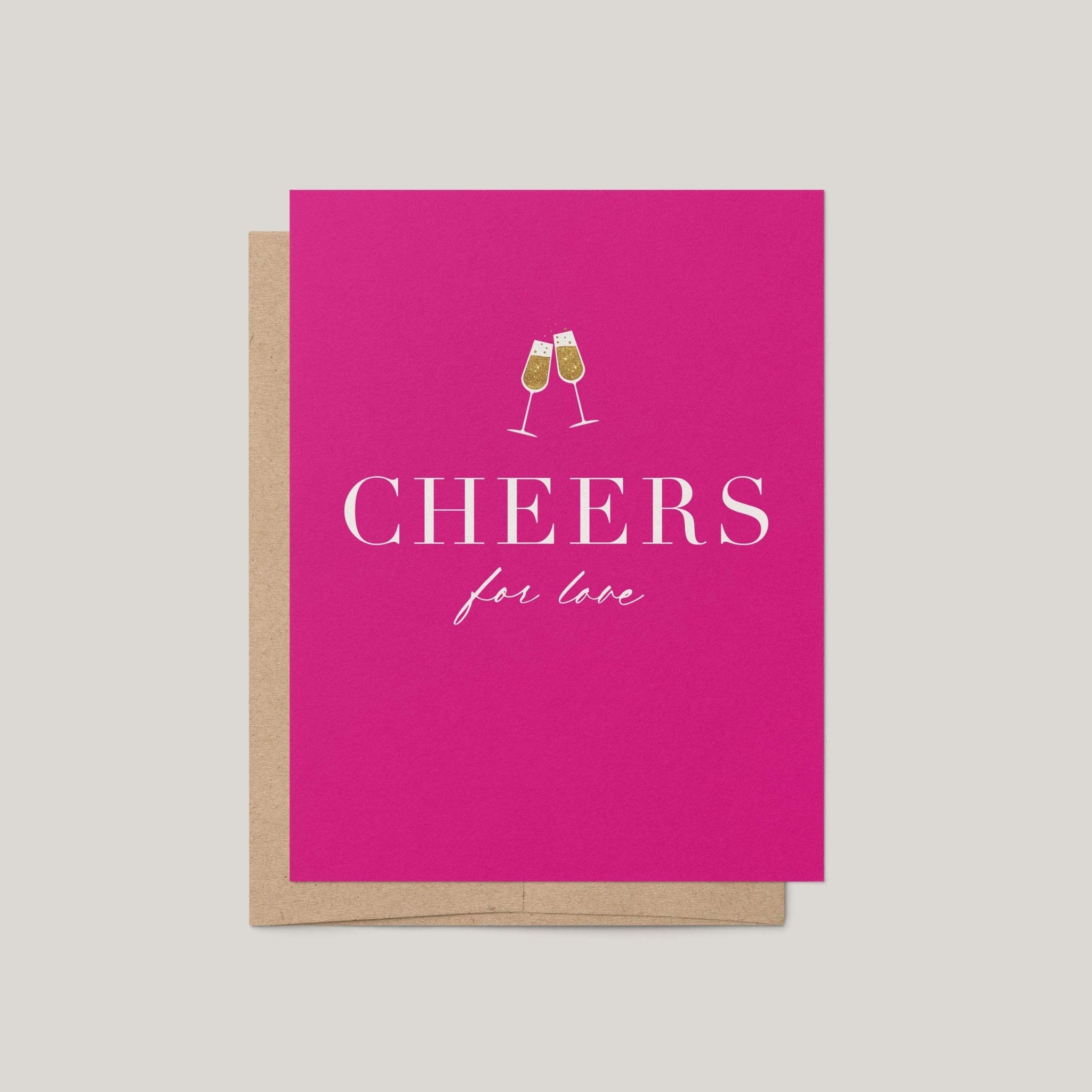 A bright pink greeting card with a kraft envelope, featuring the text 'CHEERS for love' and a small illustration of two clinking champagne glasses, shown on a light gray background.