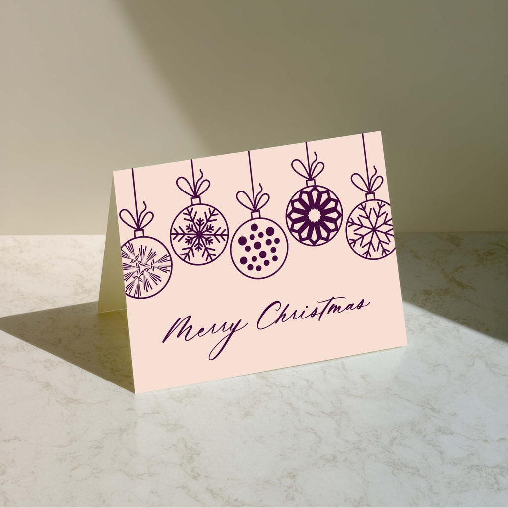 Christmas Ornaments Merry Christmas card by Blú Rose standing upright, blush card with plum ornament illustration on a neutral background