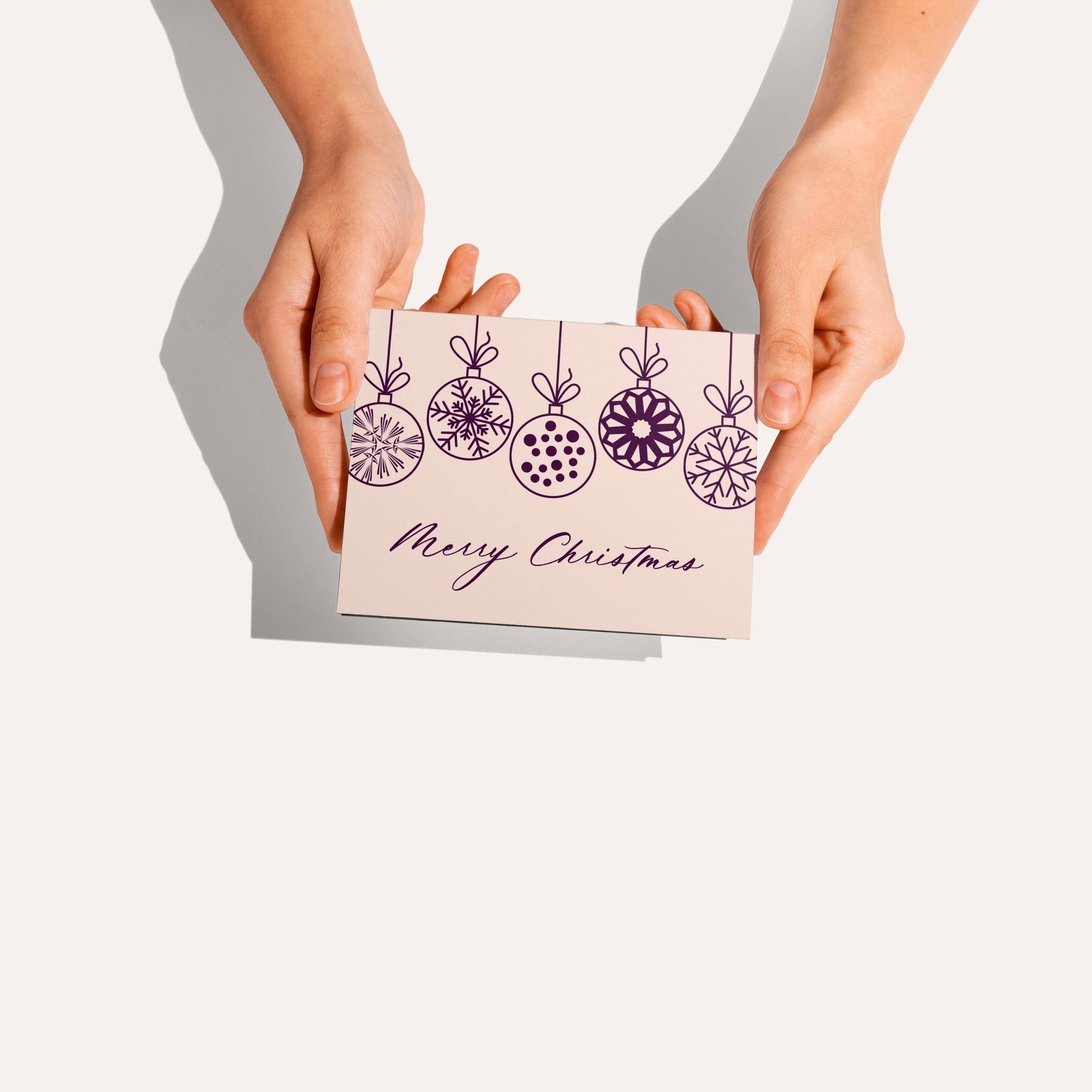 Hands holding Christmas Ornaments Greeting Card featuring plum ornaments on white background.
