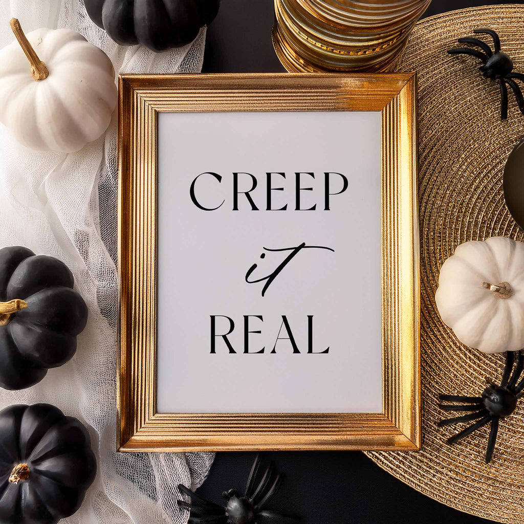 “Creep it Real” art print in a gold frame styled with white and black pumpkins and fall decor.