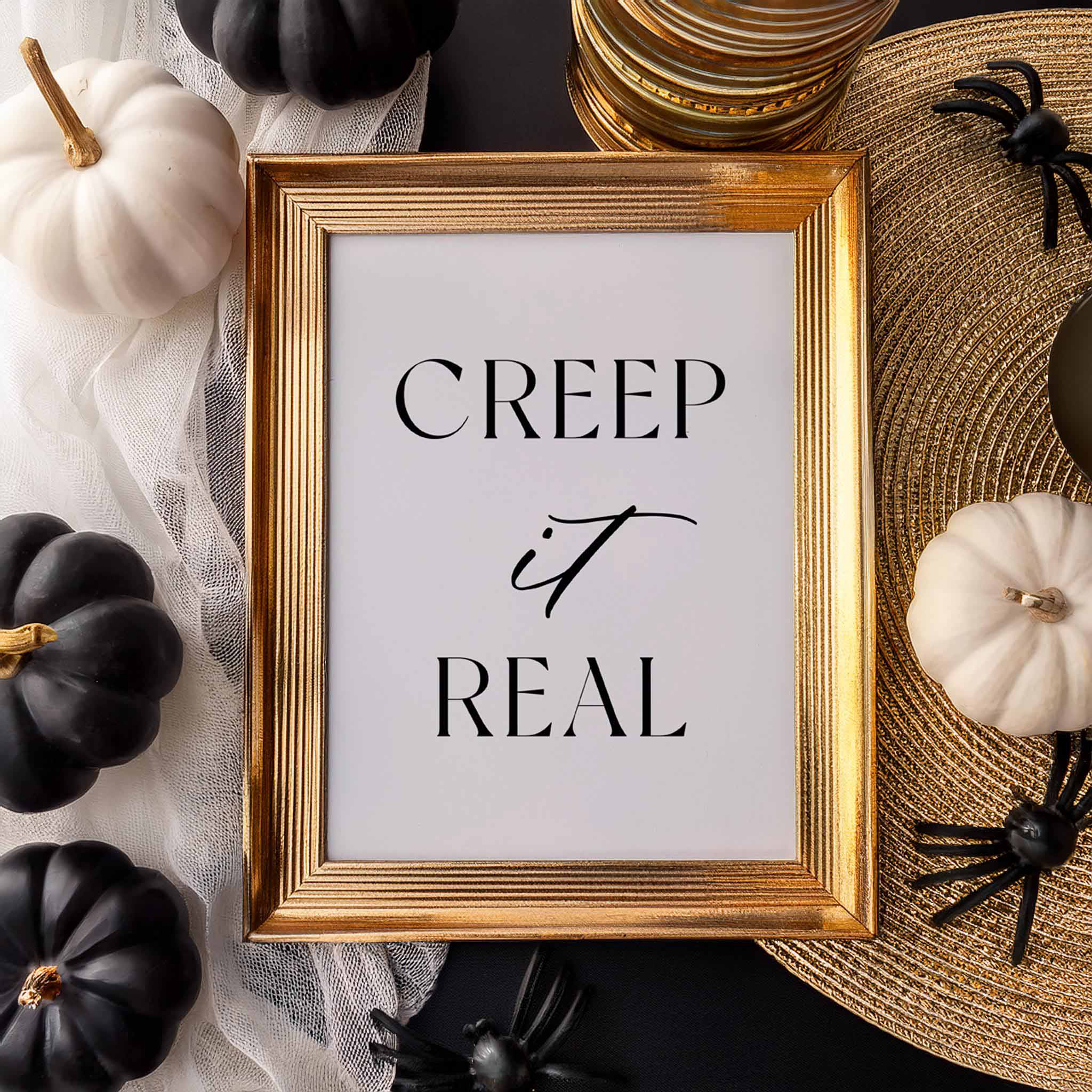 “Creep it Real” art print in a gold frame styled with white and black pumpkins and fall decor.