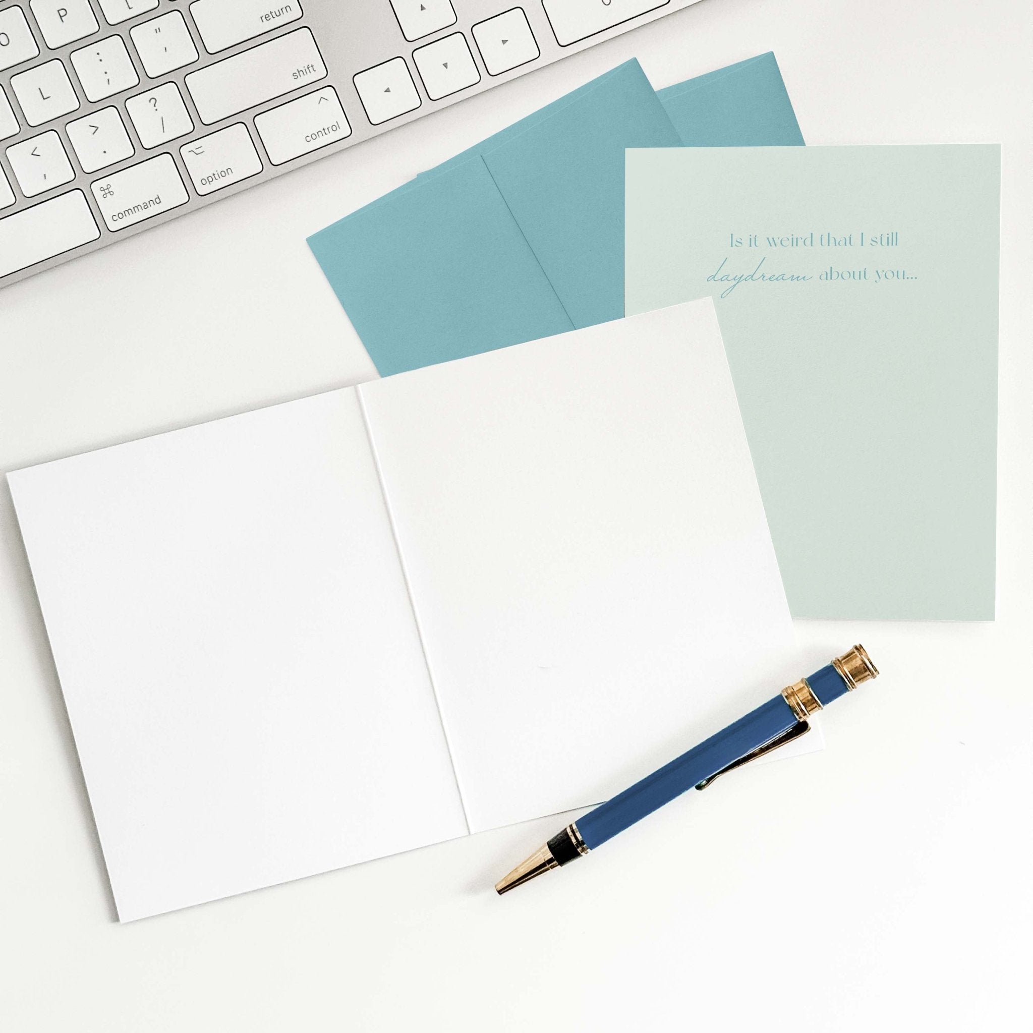 Daydream About You love card by Blú Rose shown open with blank interior, blue envelope and pen on a white desk
