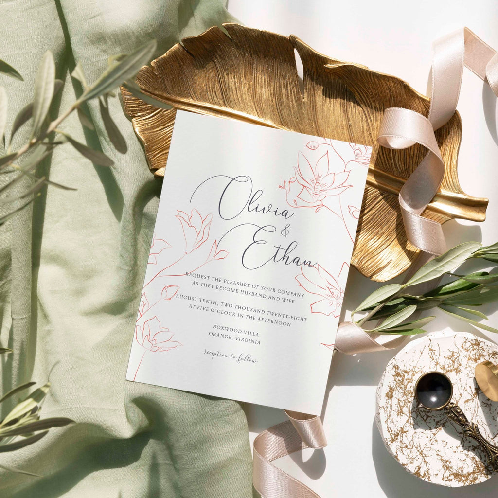 Delicate Floral wedding invitation by Blú Rose, white card with fine rose-gold line florals, styled on a gold leaf dish with sage linen and ribbon