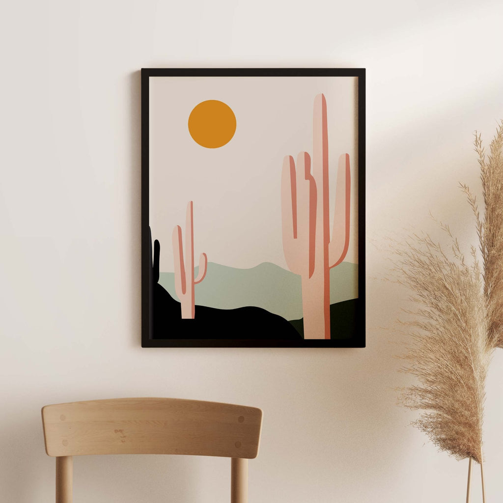 Desert Sunrise Cacti art print by Blú Rose, saguaro cactus desert scene with an orange sun in a black frame on a white wall with pampas grass
