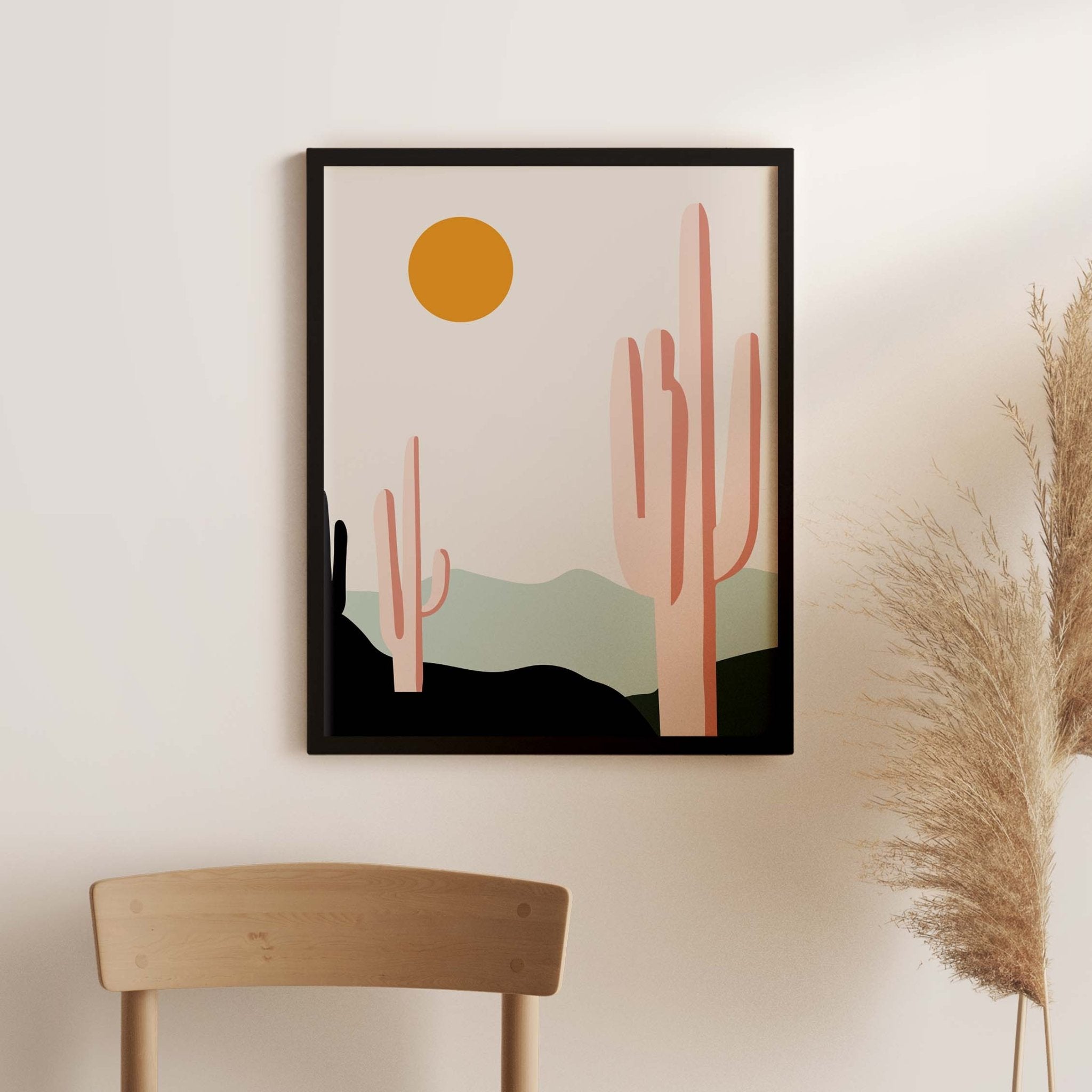 Desert Sunrise Cacti art print by Blú Rose, saguaro cactus desert scene with an orange sun in a black frame on a white wall with pampas grass