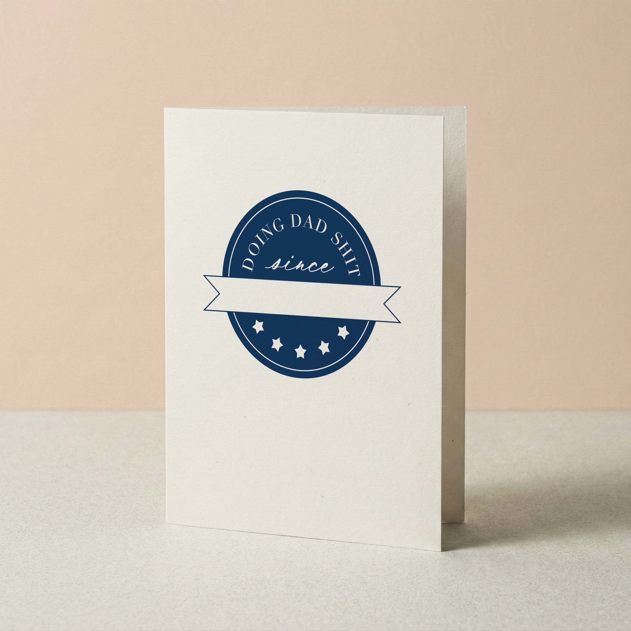 Doing Dad Shit funny dad card by Blú Rose standing upright, ivory card with navy crest on a neutral background