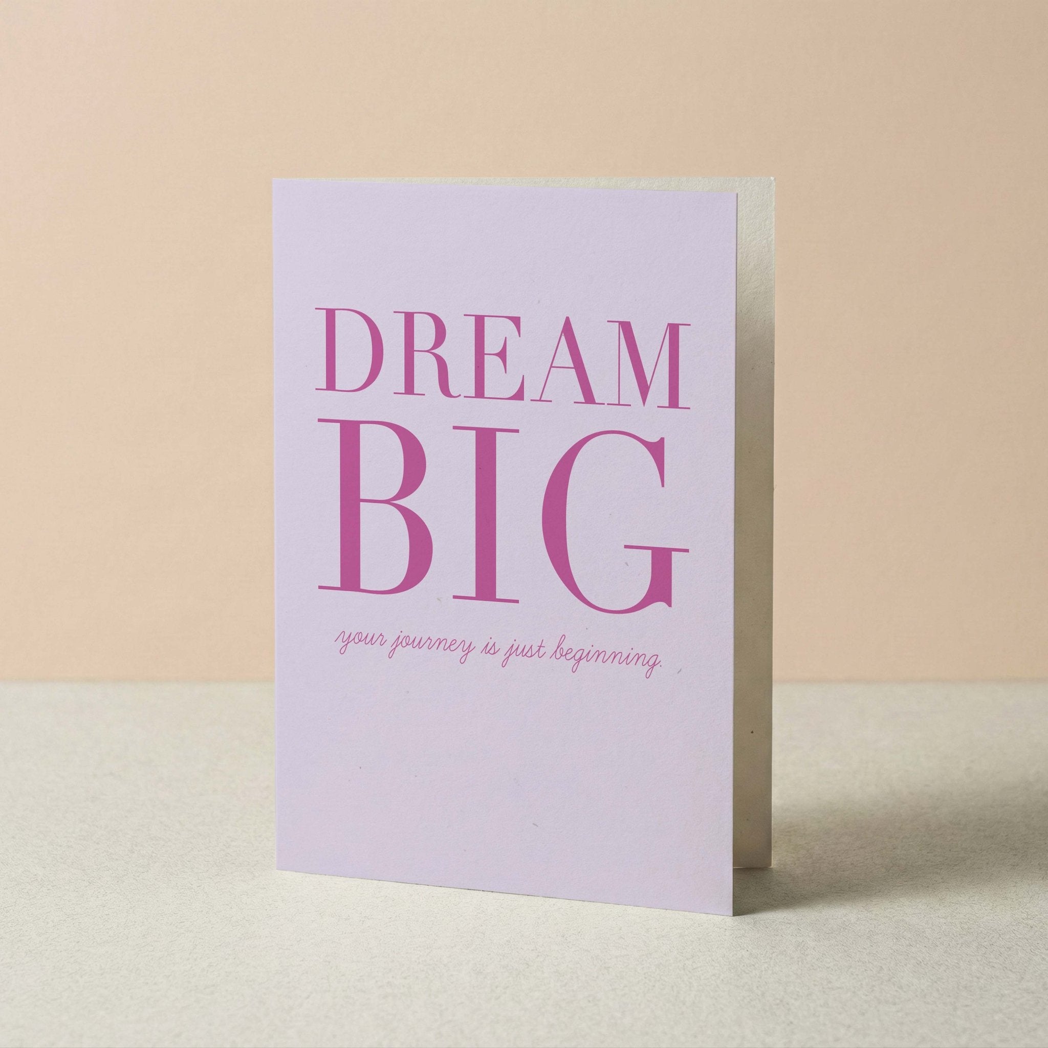 Dream Big graduation card by Blú Rose standing upright, lavender card with magenta typography on a neutral background