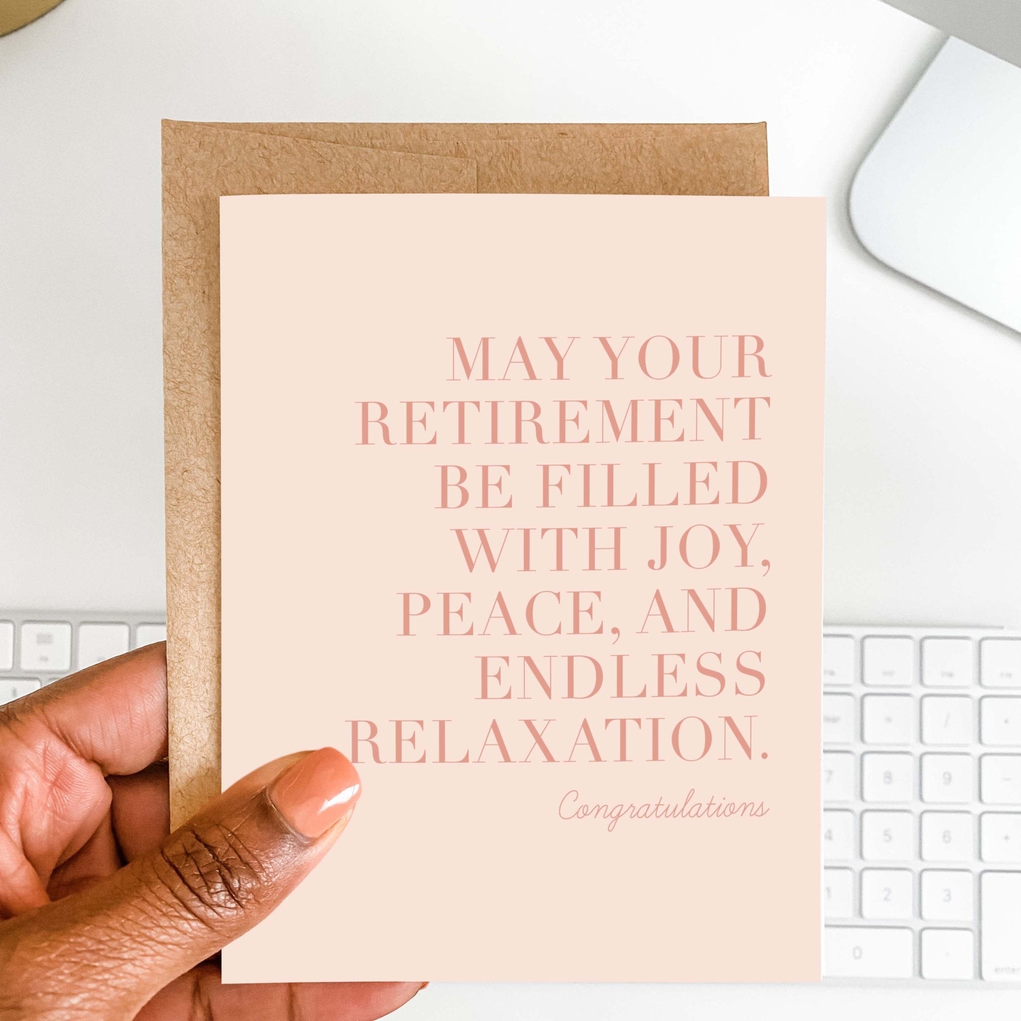 Endless Relaxation retirement card by Blú Rose held in hand over a white desk with keyboard and kraft envelope