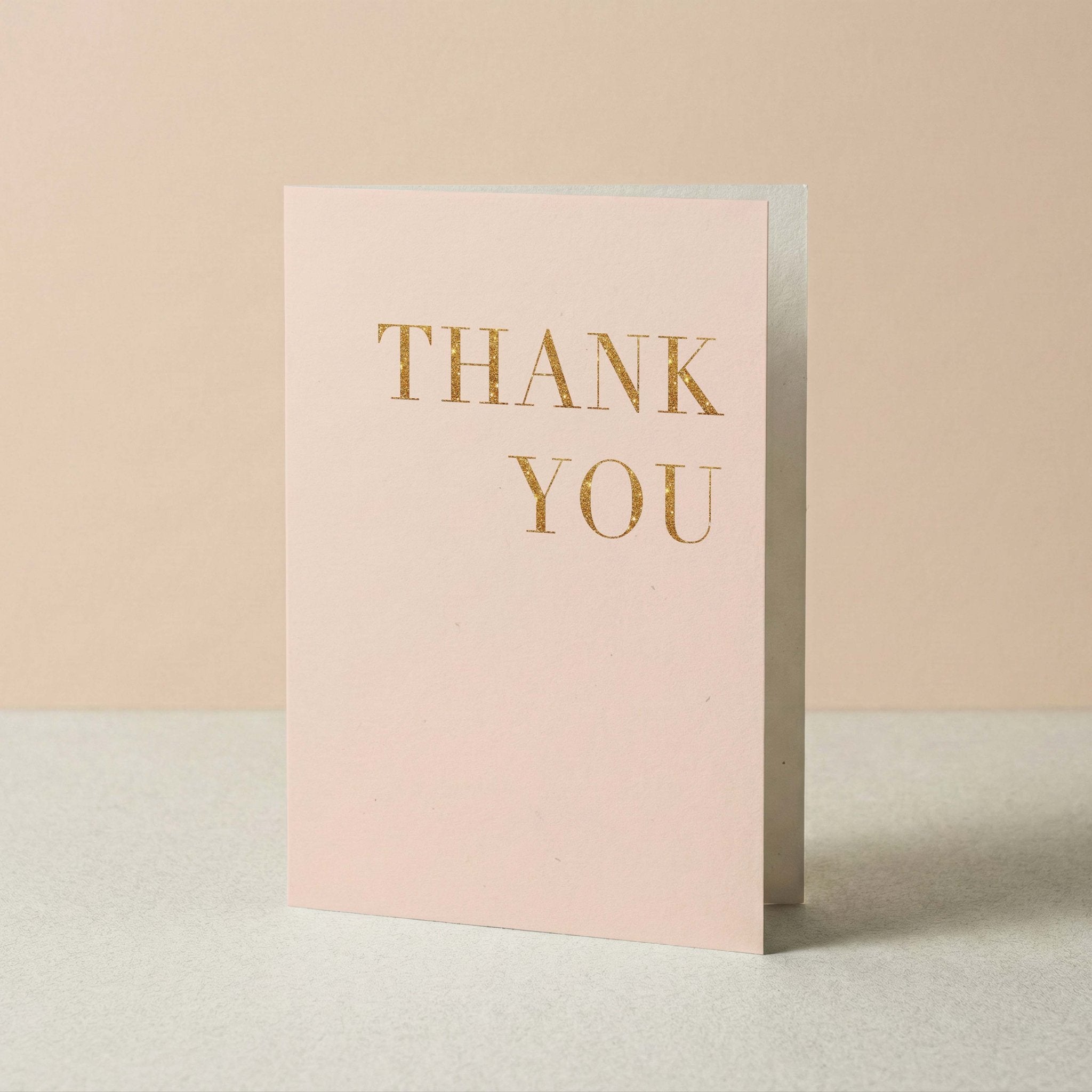 Faux Glitter Thank You card by Blú Rose standing upright, blush card with gold glitter text on a neutral background