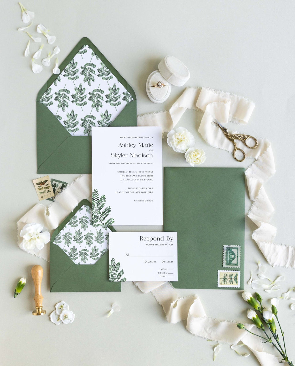 Fern wedding invitation suite by Blú Rose, invitation and response card with a green fern illustration, styled with fern-lined green envelopes, ribbon, and a wax seal