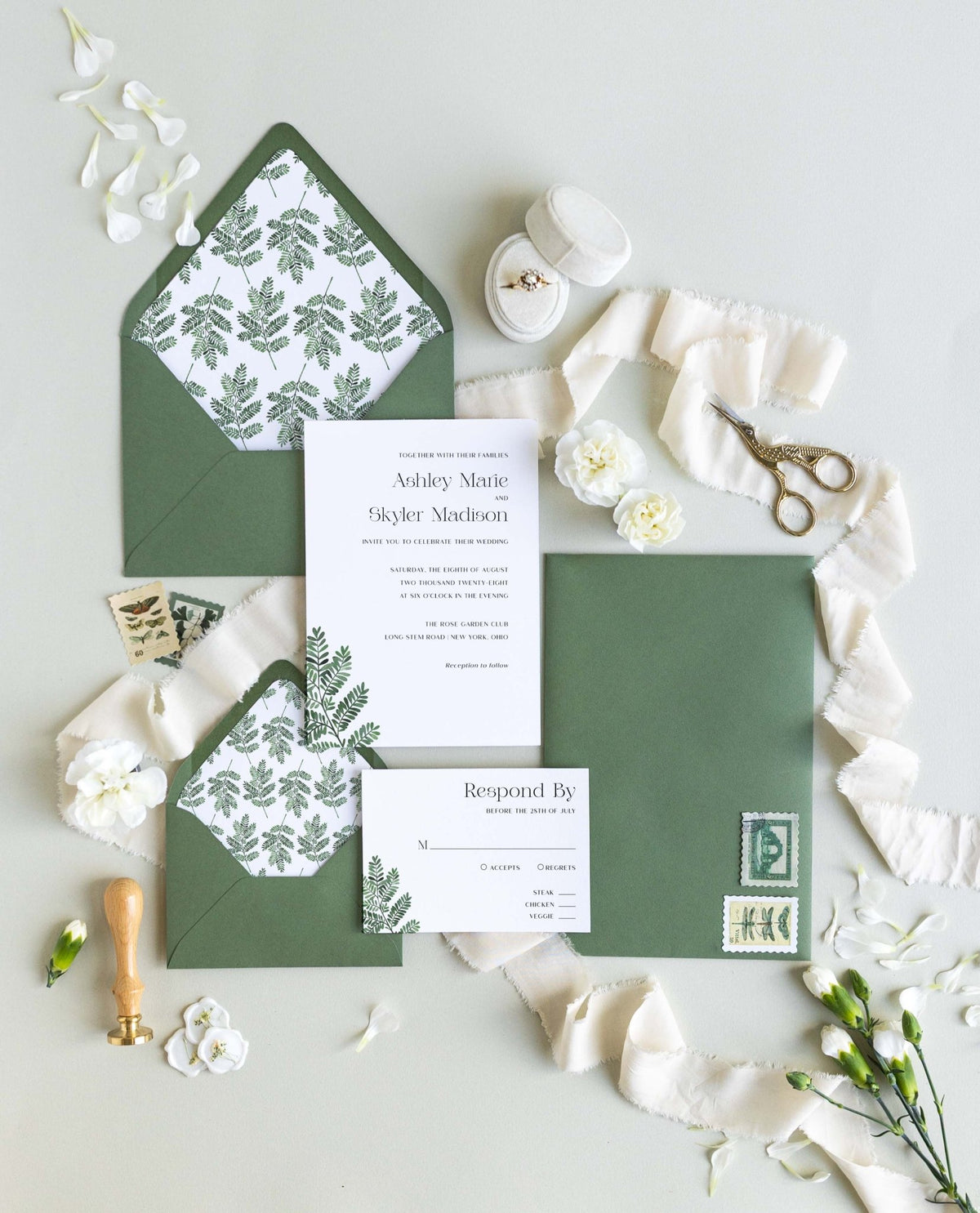 Fern wedding invitation suite by Blú Rose, invitation and response card with a green fern illustration, styled with fern-lined green envelopes, ribbon, and a wax seal