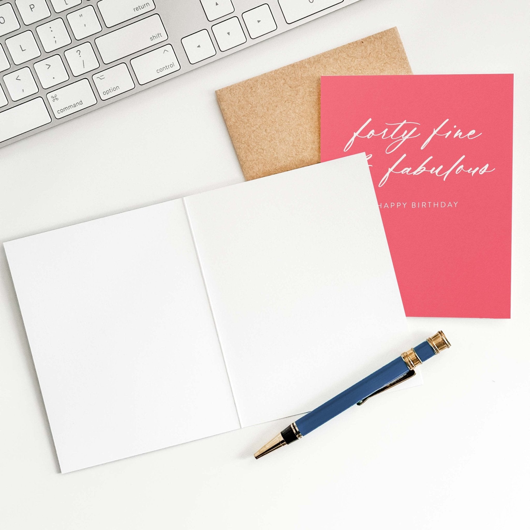 Forty Fine + Fab birthday card by Blú Rose shown open with blank interior, kraft envelope and pen on a white desk