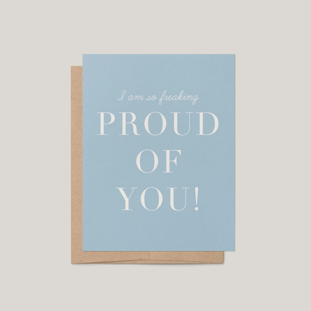 Freaking Proud of You encouragement greeting card by Blú Rose, dusty blue card with white proud of you text, shown with kraft envelope