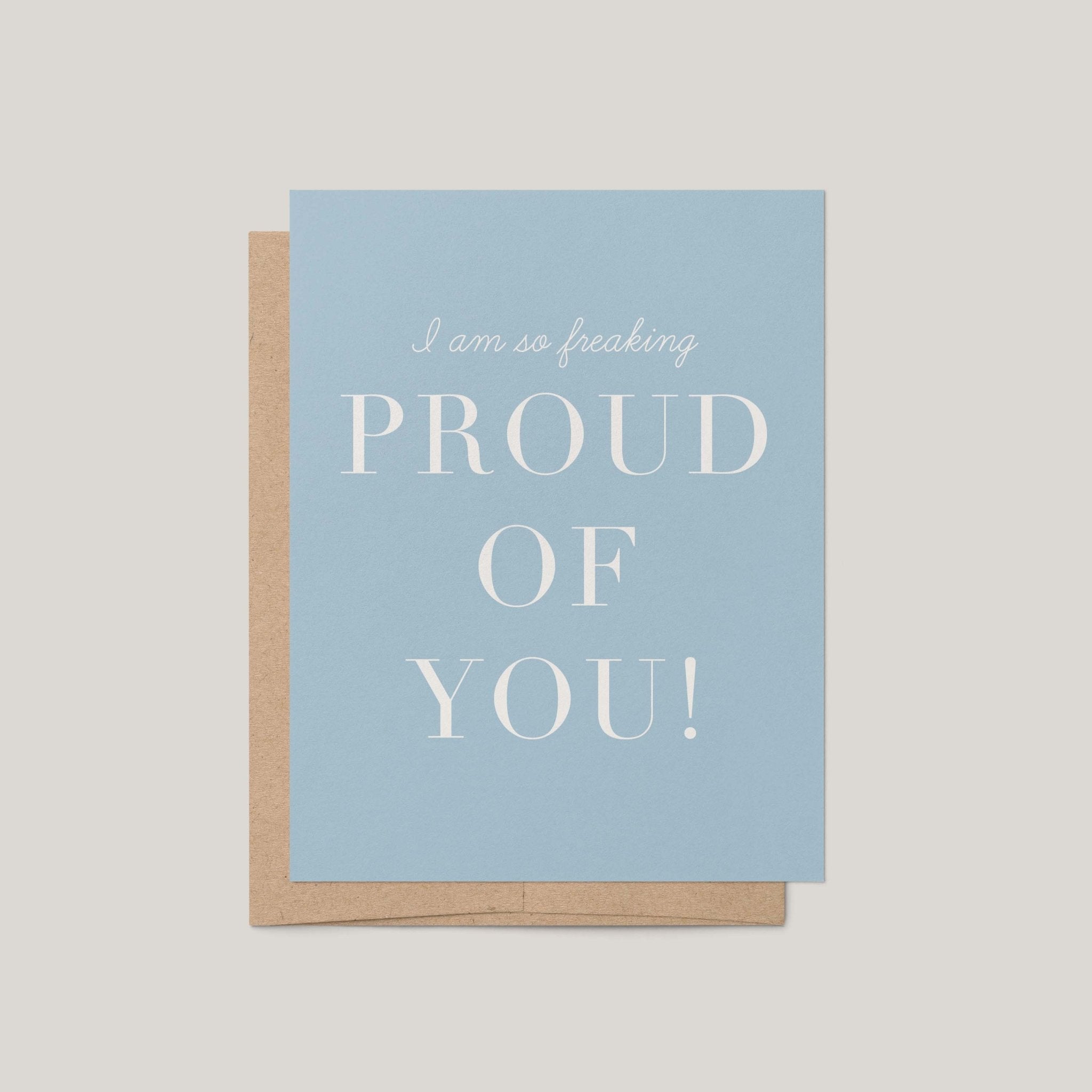 Freaking Proud of You encouragement greeting card by Blú Rose, dusty blue card with white proud of you text, shown with kraft envelope