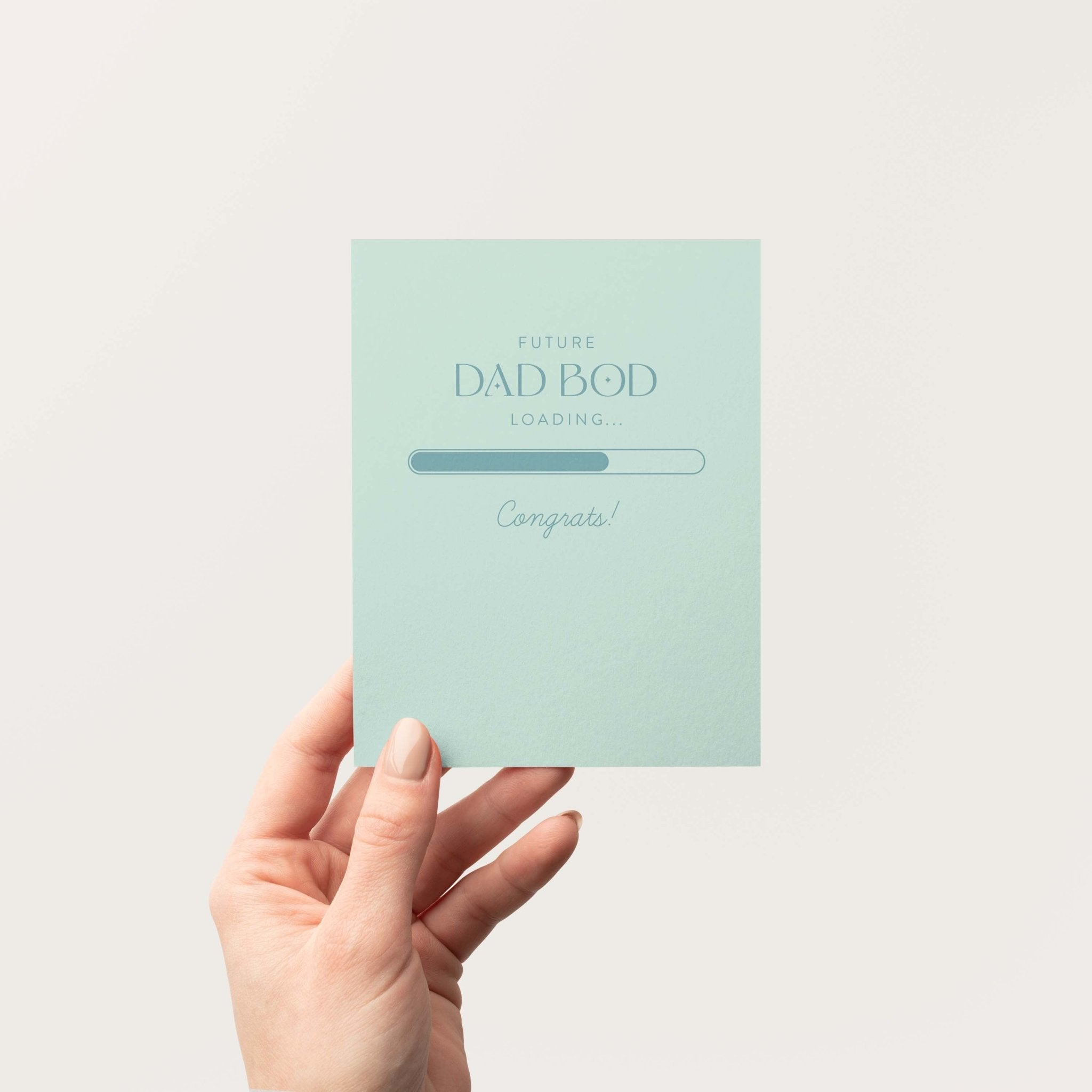 Future Dad Bod Loading new dad greeting card by Blú Rose held in hand against a neutral off-white background
