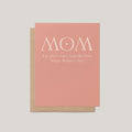 A Mother's Day greeting card with a dusty pink front and a kraft brown envelope behind it, featuring the text 'MOM I'm glad I don't look like Dad. Happy Mother's Day.