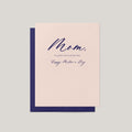 A Mother's Day greeting card with a pale blush pink front and navy blue envelope, featuring the handwritten-style text 'Mom, I'm glad I don't look like Dad. Happy Mother's Day.