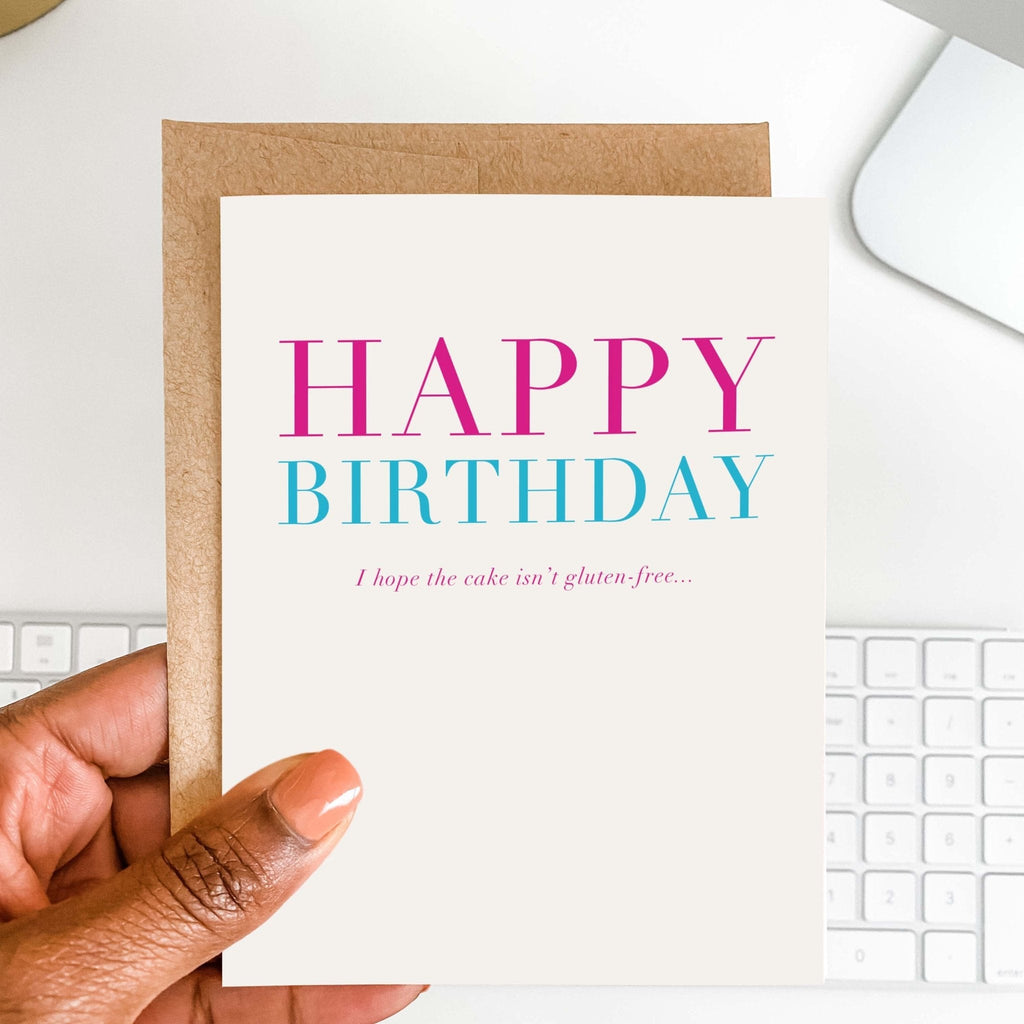 Gluten-Free Birthday funny card by Blú Rose held in hand over a white desk with keyboard and kraft envelope