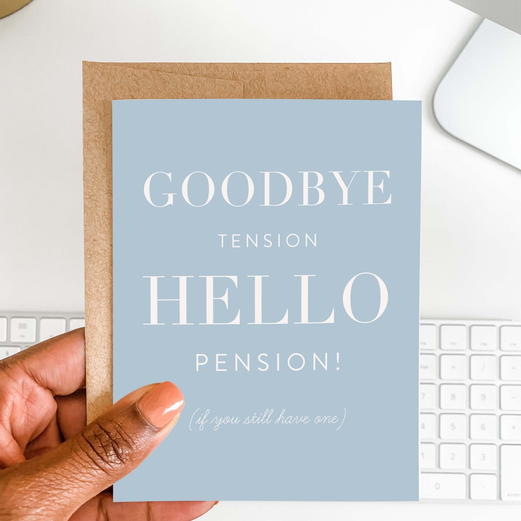 Goodbye Tension, Hello Pension retirement greeting card by Blú Rose held in hand over a white desk with keyboard and kraft envelope