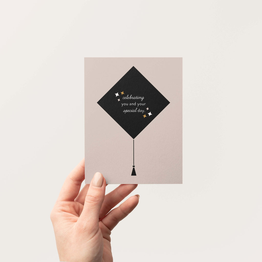 Grad Cap graduation greeting card by Blú Rose held in hand against a neutral off-white background