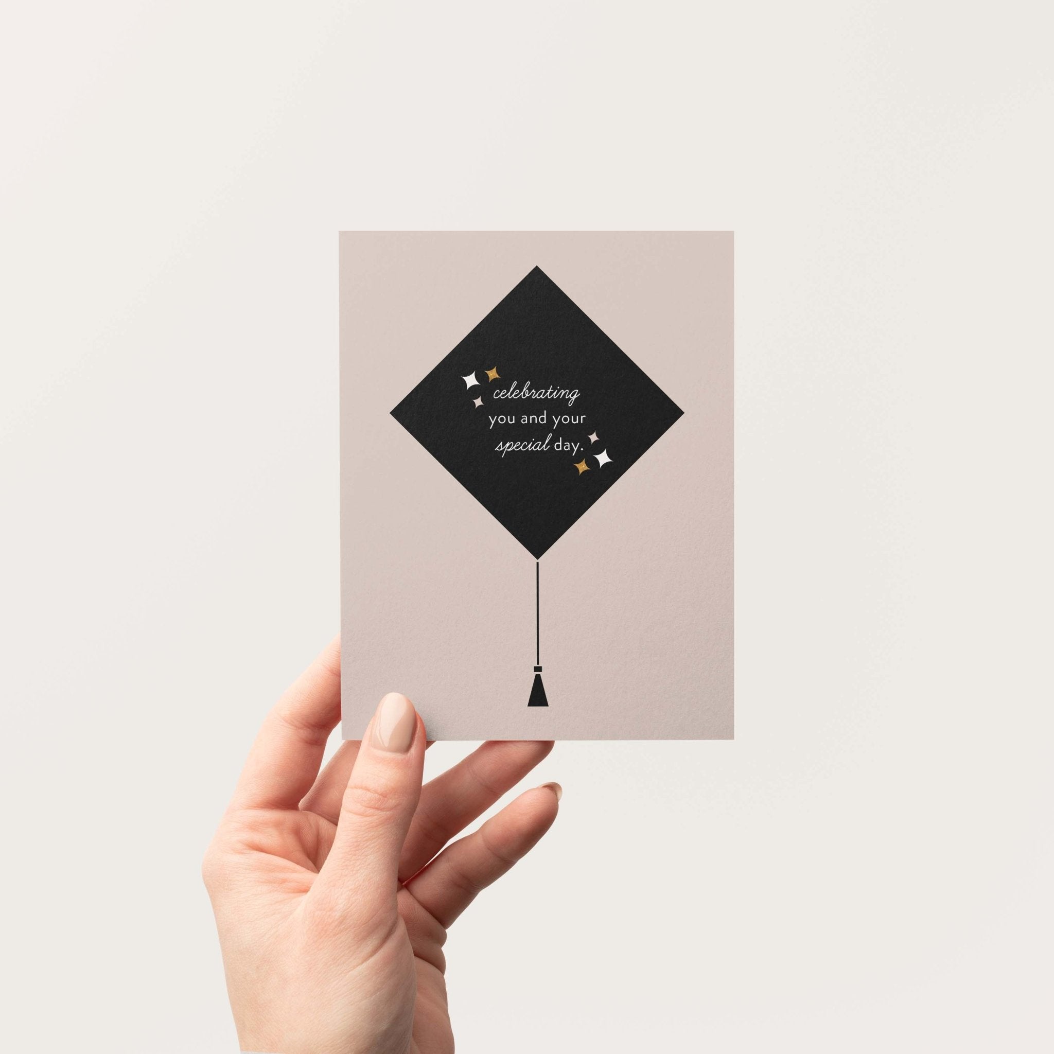 Grad Cap graduation greeting card by Blú Rose held in hand against a neutral off-white background