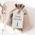 Green Sparkle Birthday gift tag by Blú Rose, white 'Happy Birthday' tag with green lettering, gold sparkles, and a candle on a burlap favor bag