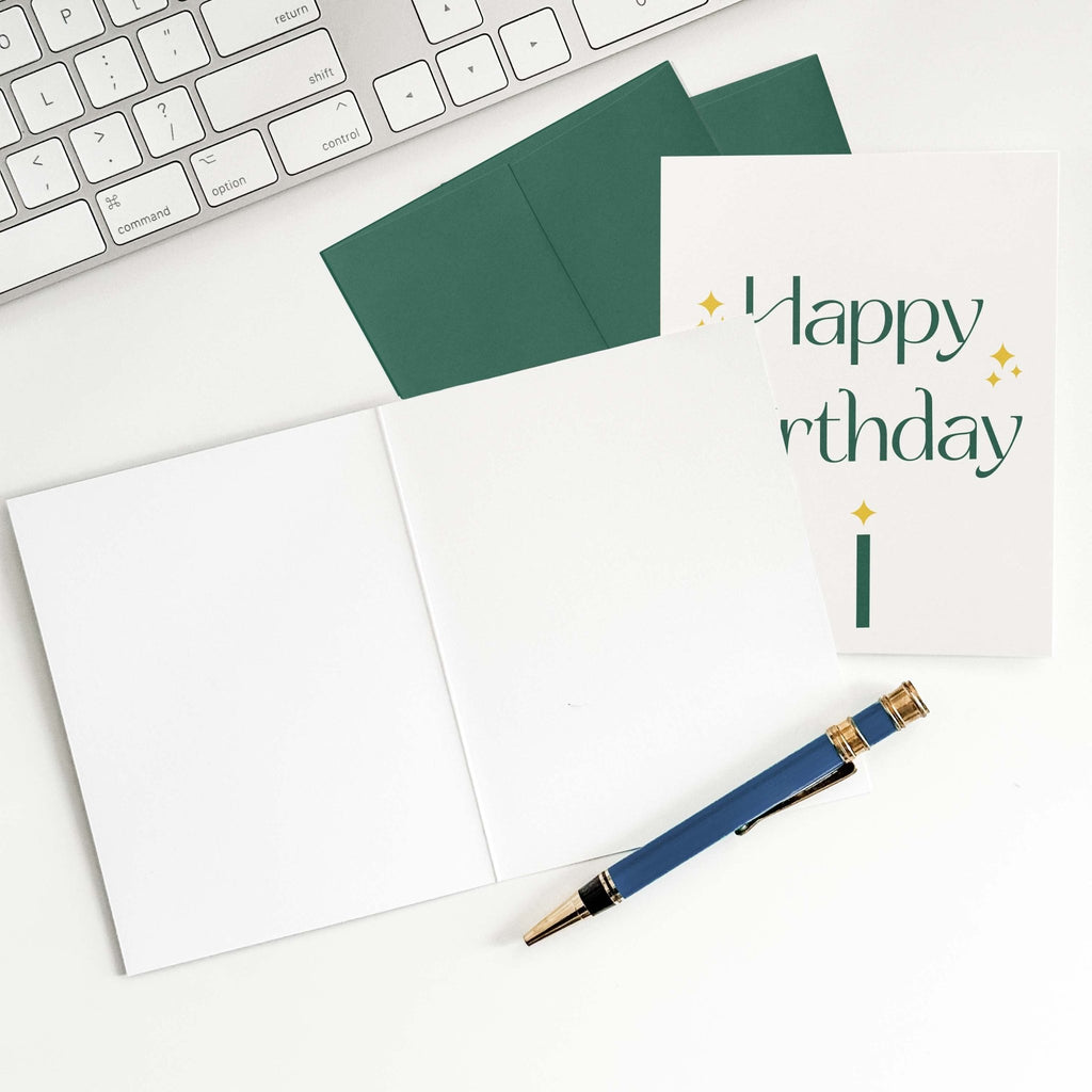 Green Sparkle Birthday card by Blú Rose shown open with blank interior, green envelope and pen on a white desk